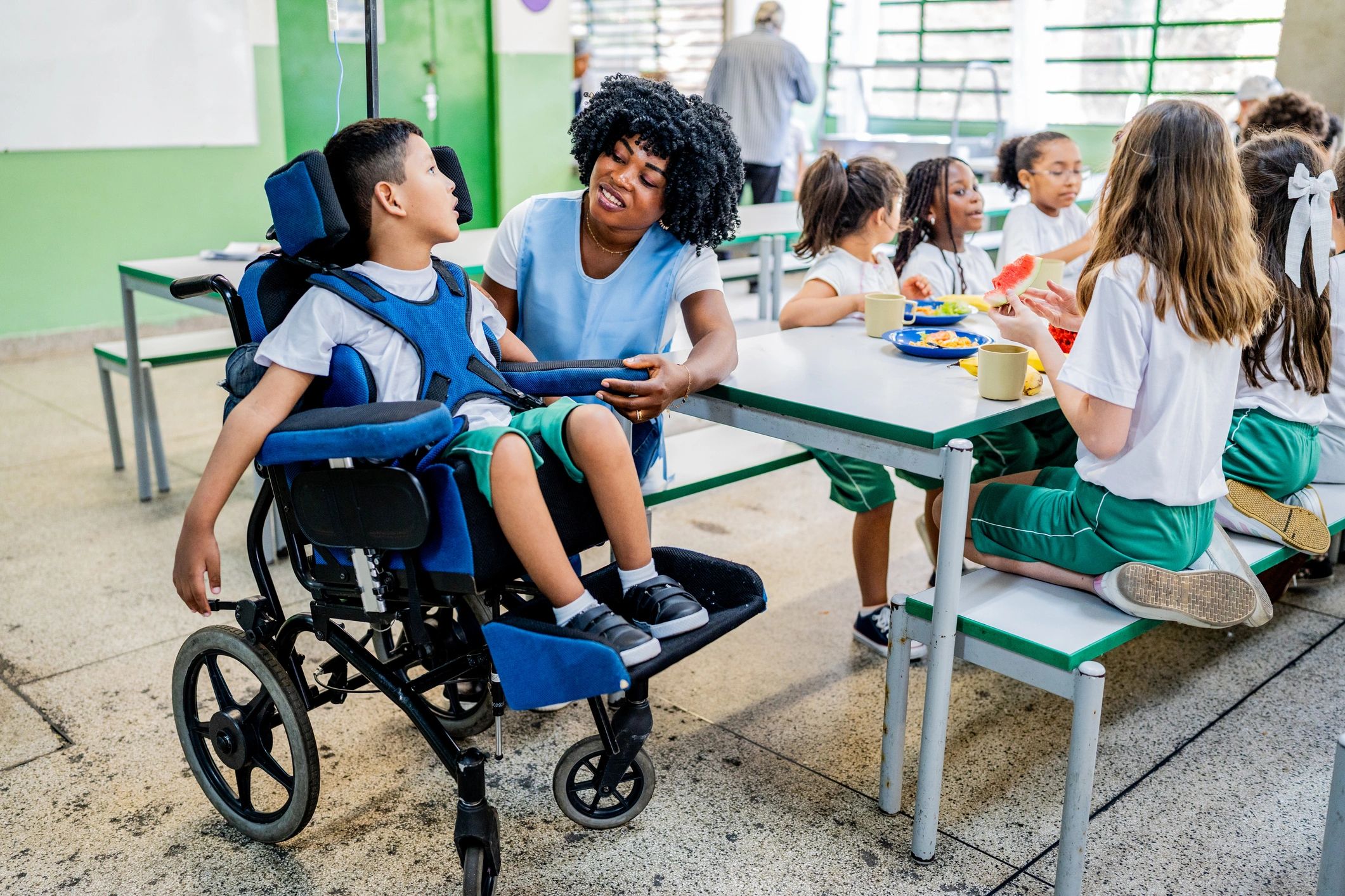 Teacher talks to schoolboy in a wheelchair during lunch in the school cafeteria